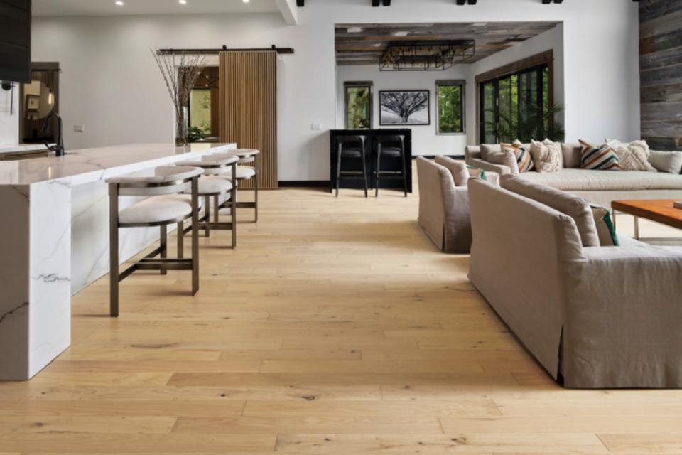 warm toned hardwood flooring in living room with grey couches and marble stone bar.